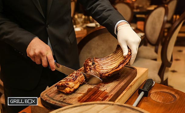 Manos de un hombre cortando unas costillas asadas sobre tabla de madera